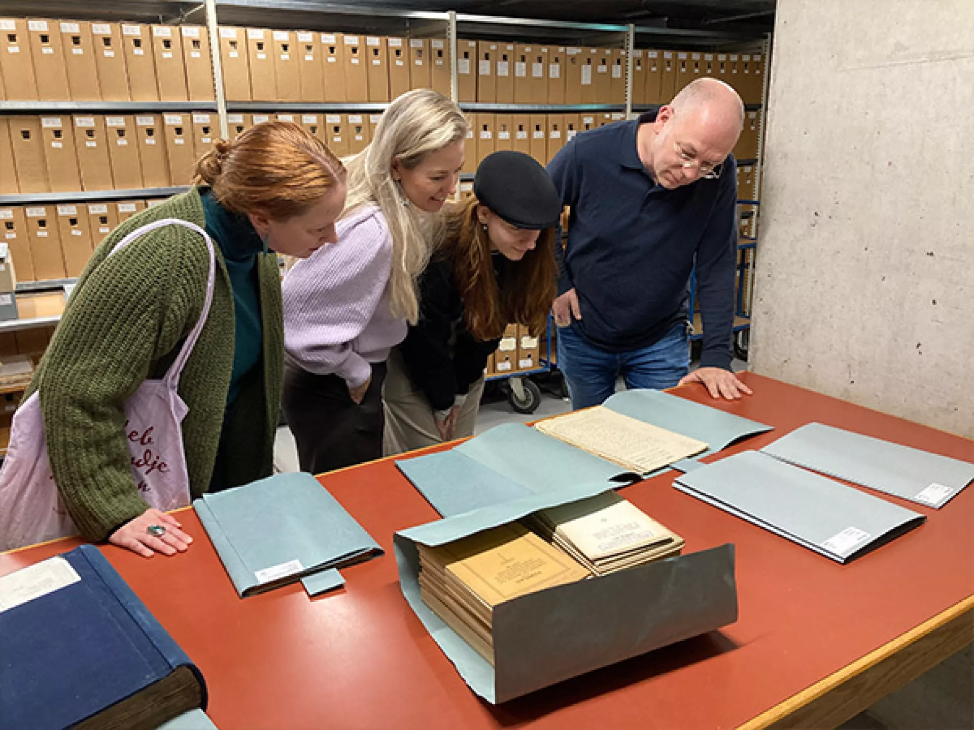 Werknemer Drents Archief geeft rondleiding in depot. Drie vrouwen buigen zich over een archiefstuk. Op de achtergrond is een depot-kast te zien.