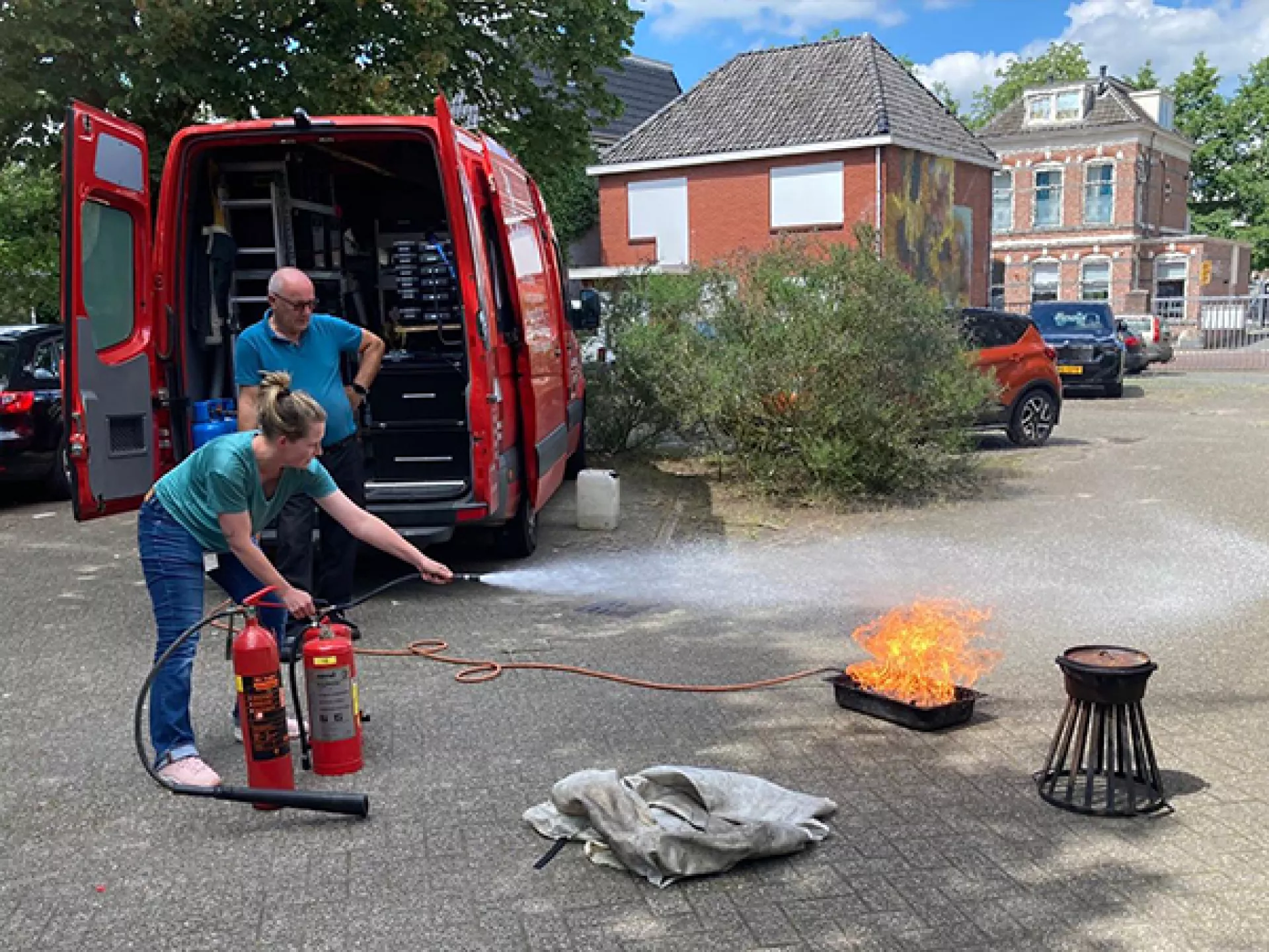 Vrouw blust brandje met brandblusser tijdens een BHV training. De trainer kijkt vanaf de zijkant toe.
