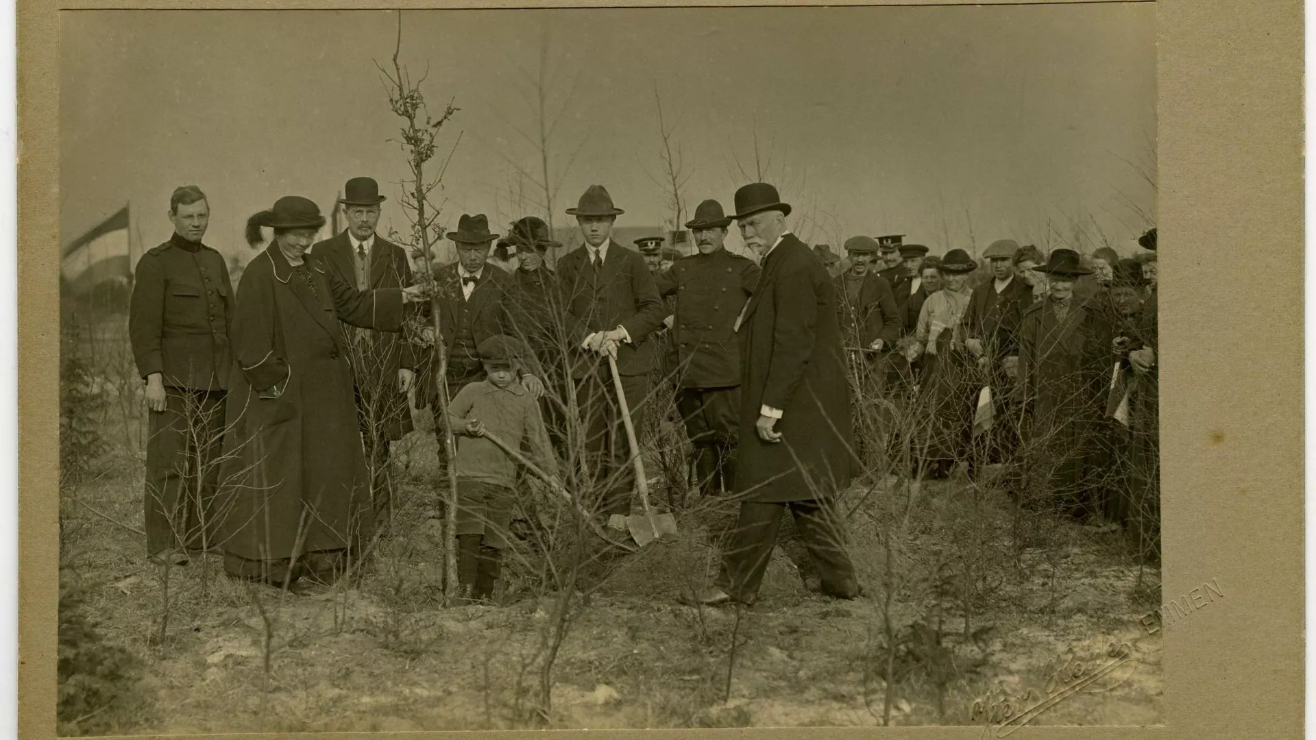 Zwart-wit foto, groep mannen en 1 vrouw, zij houdt een boom vast en is Hnedrika van Riel-Smeenge. Een man en kind graven een gat voor de boom.