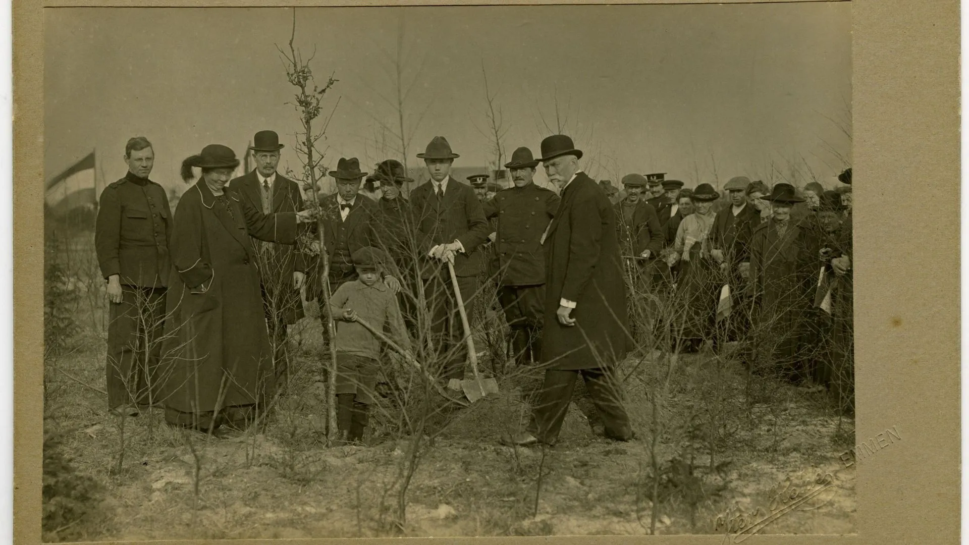 Zwart-wit foto, groep mannen en 1 vrouw, zij houdt een boom vast en is Hnedrika van Riel-Smeenge. Een man en kind graven een gat voor de boom.