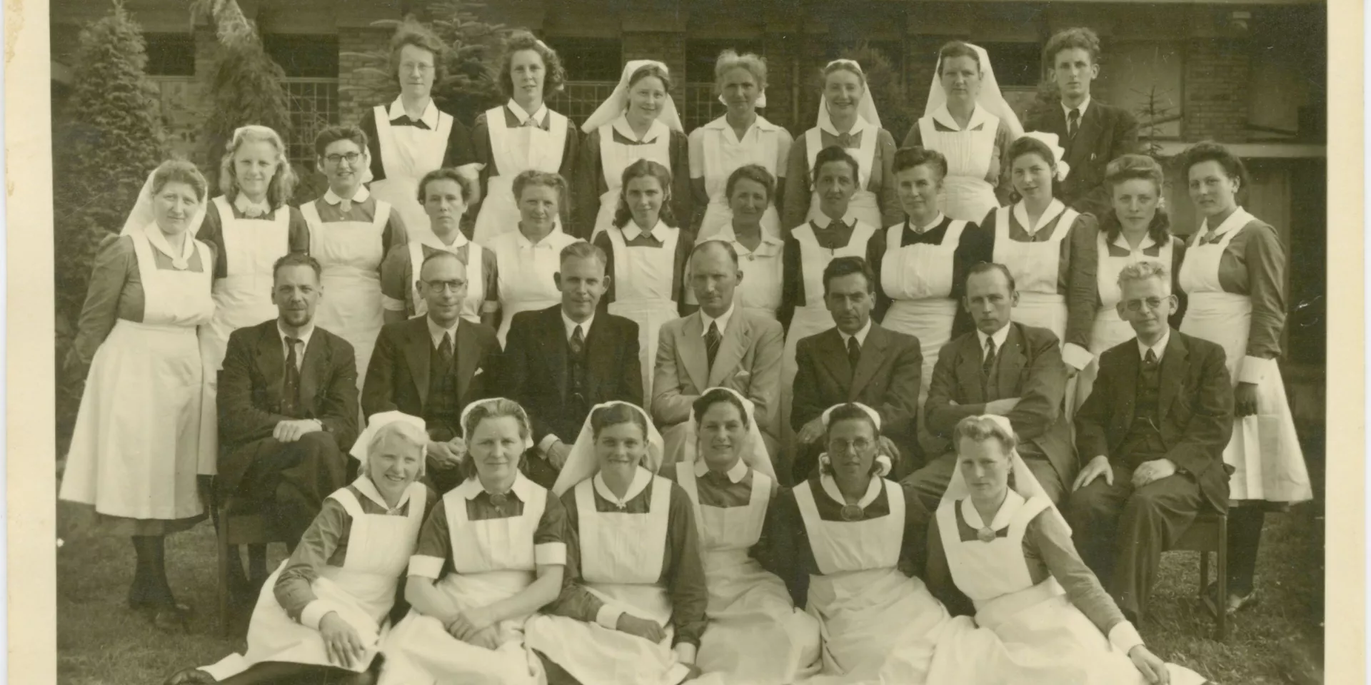 Groepsfoto met verpleegkundigen en doktoren. Er staan vier rijen met personen op de foto. Vooraan 6 vrouwen, daarachter 7 mannen in pak. Daarachter nog twee rijden met vrouwen