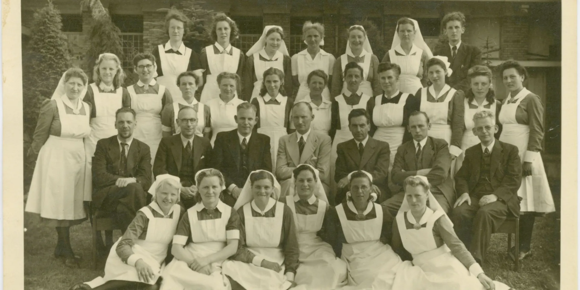 Groepsfoto met verpleegkundigen en doktoren. Er staan vier rijen met personen op de foto. Vooraan 6 vrouwen, daarachter 7 mannen in pak. Daarachter nog twee rijden met vrouwen