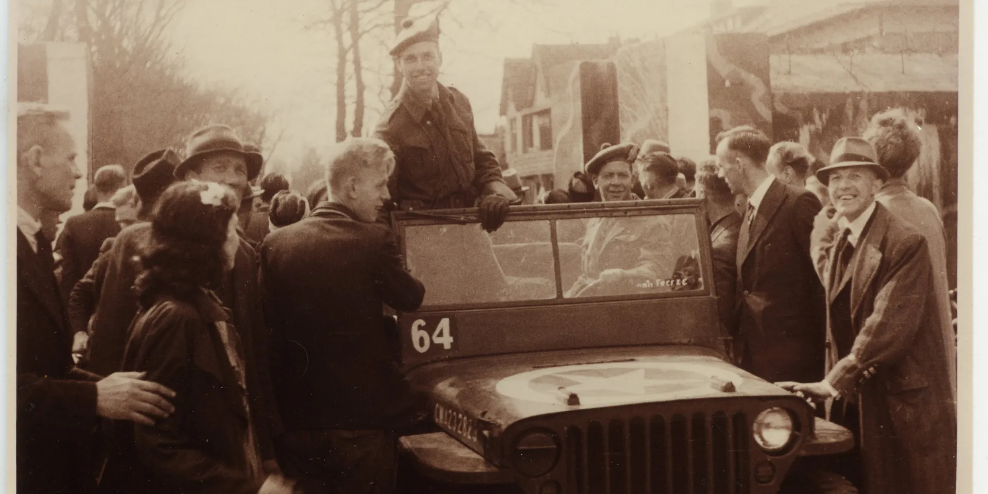 Foto van bevrijding in Drenthe, vrolijke mensen, jeep in het midden met lachende militair