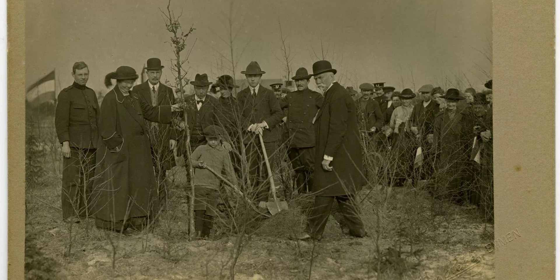 Zwart-wit foto, groep mannen en 1 vrouw, zij houdt een boom vast en is Hnedrika van Riel-Smeenge. Een man en kind graven een gat voor de boom.