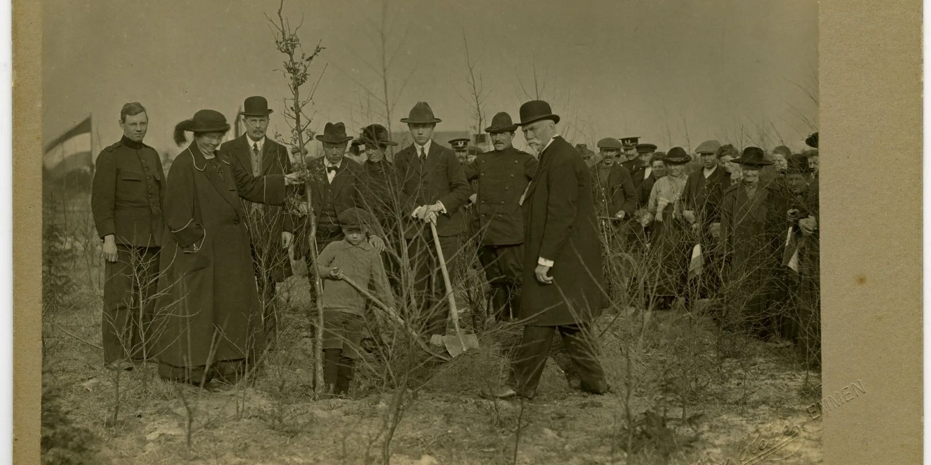 Zwart-wit foto, groep mannen en 1 vrouw, zij houdt een boom vast en is Hnedrika van Riel-Smeenge. Een man en kind graven een gat voor de boom.